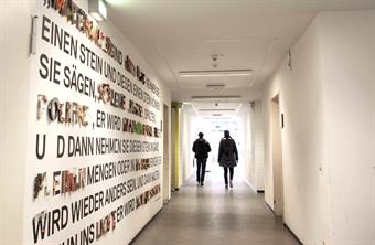 Two students are walking down a bright hallway of HSD. The left wall is decorated with lettering made of different materials.